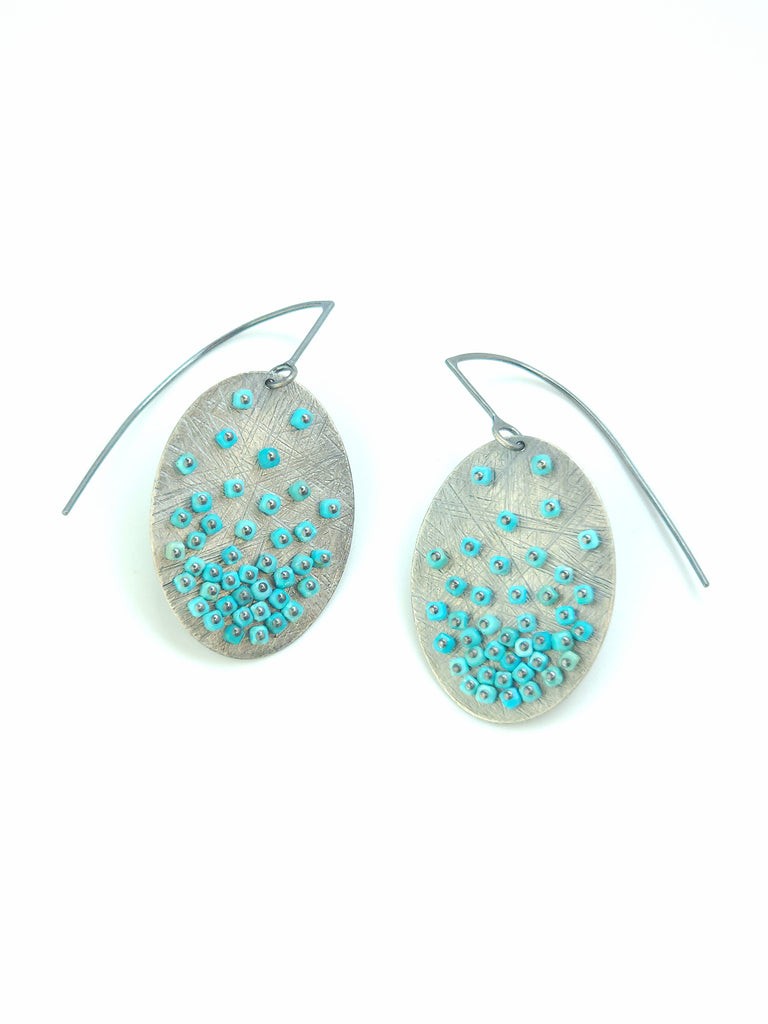 Oval-shaped earrings with turquoise bead embellishments on a white background