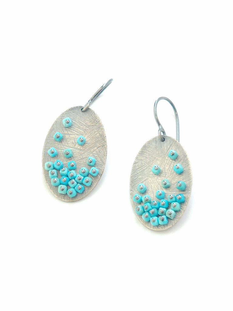 Oval-shaped earrings with textured surface and turquoise bead details on a white background